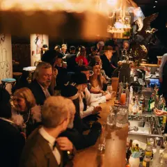 Goście w stylu retro bawią się w restauracji z muzyką na żywo w Warszawie. Przy barze panuje gwar, a atmosfera jest gorąca.
