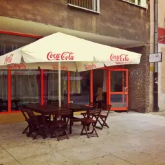 Tanie jedzenie Wrocław Rynek: stoliki pod parasolem Coca-Cola, wejście do lokalu, rowery przy ścianie.