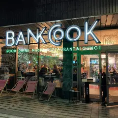 Nietypowe restauracje Poznań: neonowy szyld "BANKOOK" nad wejściem do lokalu z ogródkiem i stolikami w środku.