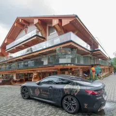 Luksusowy hotel Górski Diament z nowoczesną architekturą i przeszklonymi balkonami. Przed budynkiem stoi elegancki samochód z motywem "Księstwo Góralskie".