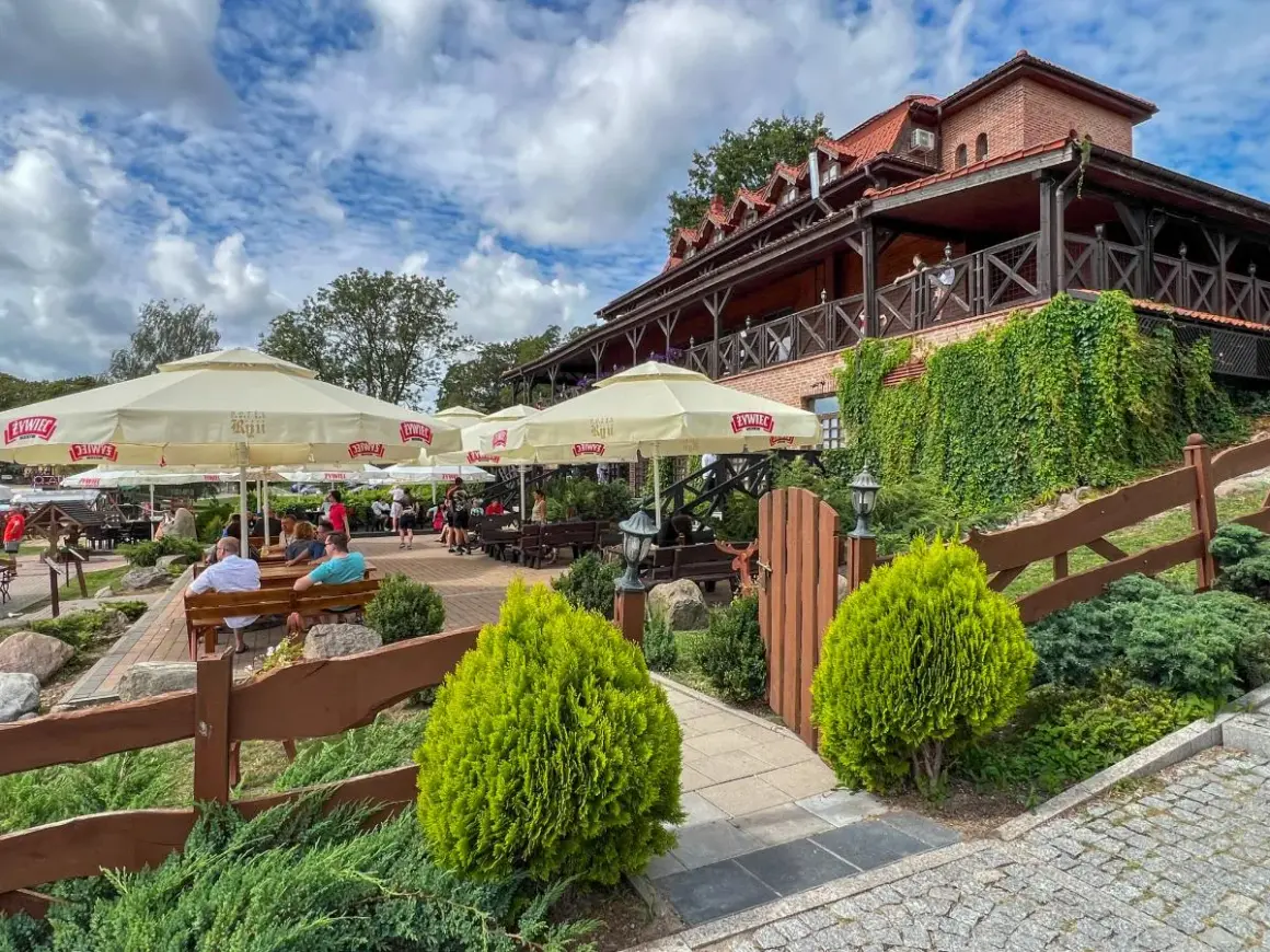 Odkryj najlepsze restauracje na Mazurach! Letni ogródek z widokiem na jezioro, gdzie można delektować się posiłkiem pod parasolami.