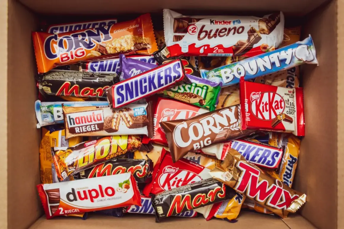 Pudełko pełne słodyczy: Snickers, Mars, Twix, Bounty, Kinder Bueno, Corny, Duplo i inne popularne polskie marki słodyczy.