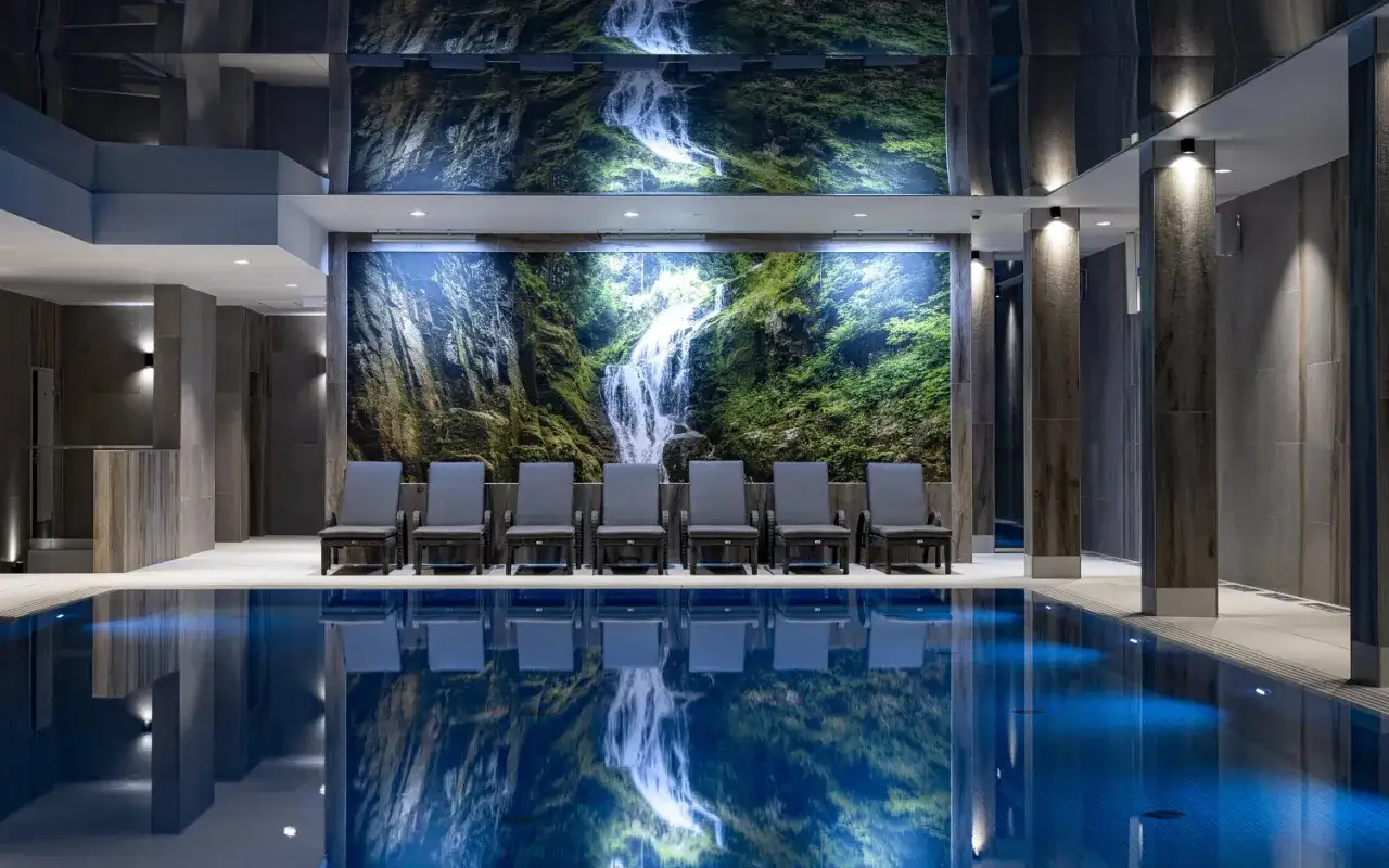 Relaks przy basenie w Platinum Mountain Hotel & Spa. Woda odbija malowniczy wodospad na ścianie.