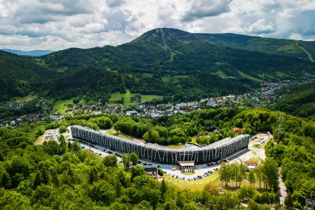 Nowoczesny Mercure Szczyrk Resort w otoczeniu zielonych Beskidów, z widokiem na górę Skrzyczne.